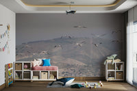 Birds are depicted soaring or flying in the sky above the hills.
