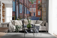 Quaint village lane wall mural with brick buildings for home decor.