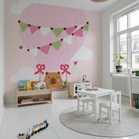 Pink bows and leafy sprigs on cartoon balloon basket artwork wall mural in playroom.