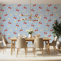 Blue gingham repeat wallpaper with illustrated red cherry pairs and white daisy motifs.