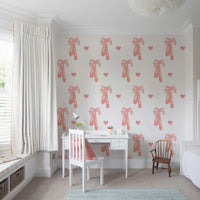 Looped pink ribbon bow beside ballet shoes on a white wallpaper.