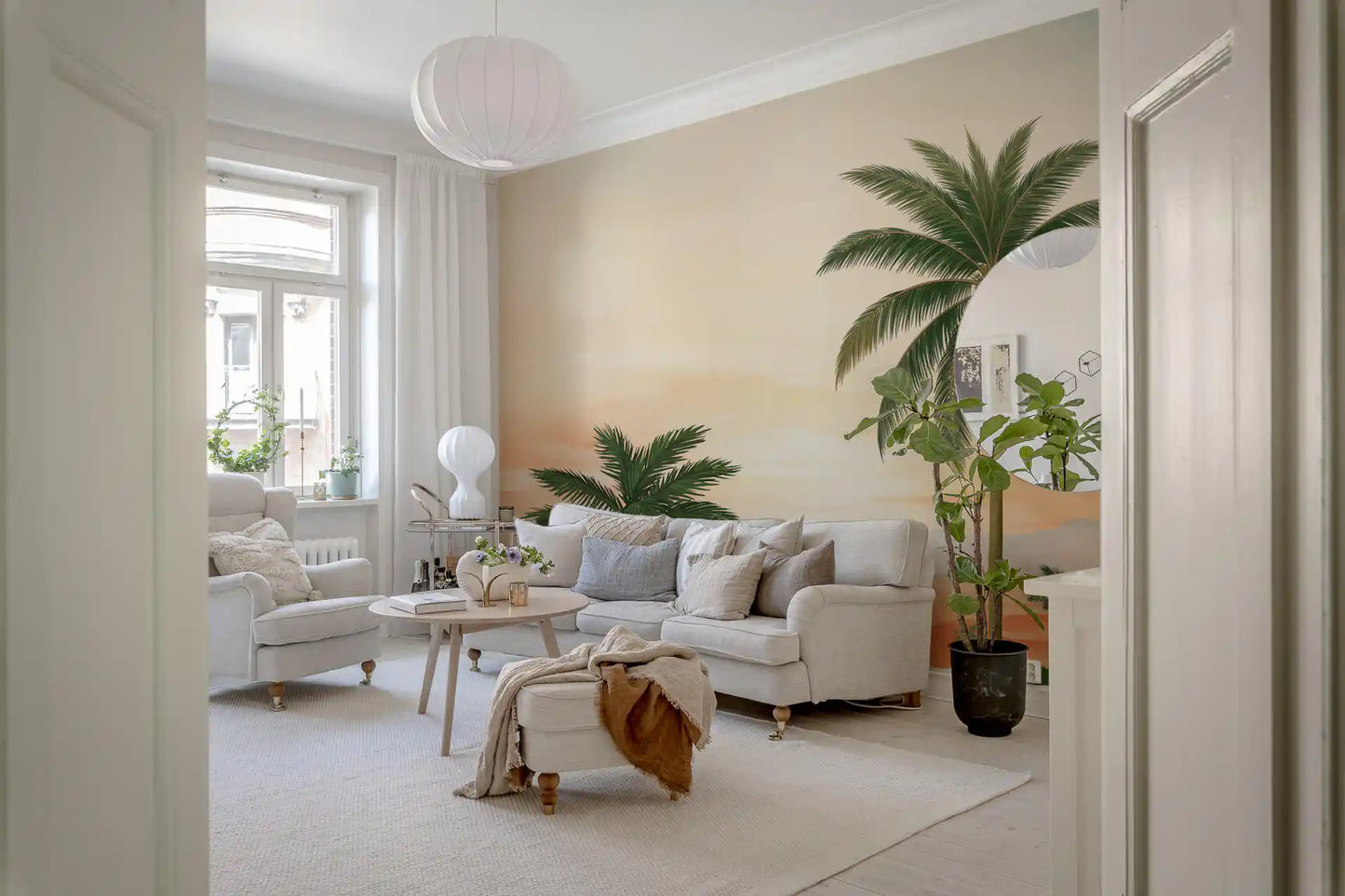 Layered coral and lavender hills behind green foliage in a tropical wall mural for living room.
