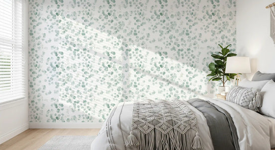Sage leaf wallpaper on a sunlit bedroom wall with grey and cream bedding GD12336