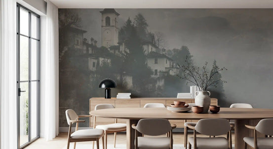 Foggy hillside village mural in a dining room with a wooden table and black lamp GD12893